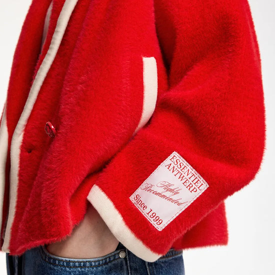 A close-up of a person wearing a bright red fuzzy jacket with cream-colored trim and a visible patch on the sleeve. The person is also wearing blue jeans, set against a plain white background.
