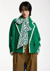 A model wearing a green fuzzy cropped cardigan with cream piping, a green and white leopard-print bow tie-neck blouse, and brown trousers, photographed against a plain white studio background.