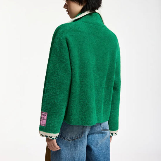 A model shown from the back wearing a bright green fuzzy knit cardigan with white ribbed trim and a pink patch on the sleeve, paired with blue jeans against a plain white background.