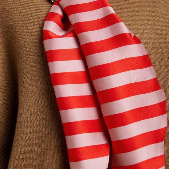 A close-up of a red and white striped silk scarf tied in a knot with a rhinestone-embellished band, resting against a brown textured fabric background.