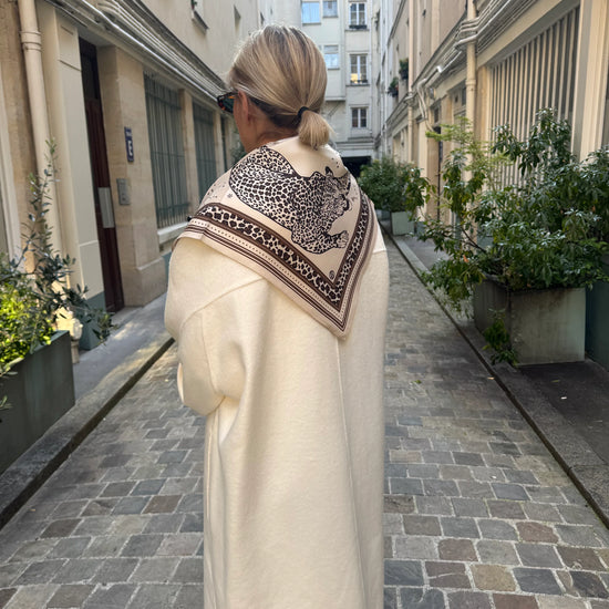 Woman walking down a narrow street wearing a long coat and patterned scarf.