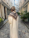 Woman walking down a narrow street wearing a long coat and patterned scarf.