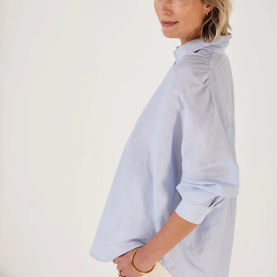 Woman wearing Mondo Corsini blue and white Pinstripe blouse on a white background. Other side view