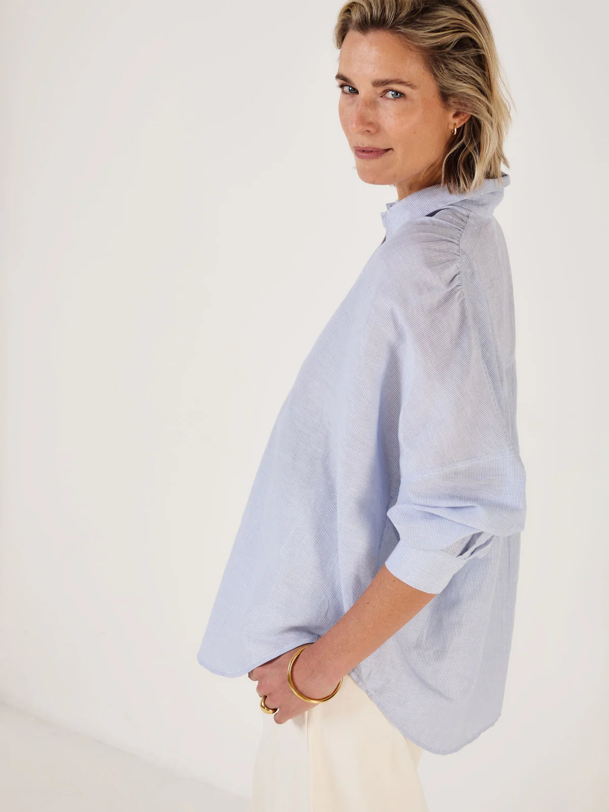 Woman wearing Mondo Corsini blue and white Pinstripe blouse on a white background. Other side view