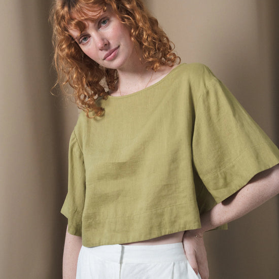 Woman wearing a green top and white pants against a beige background