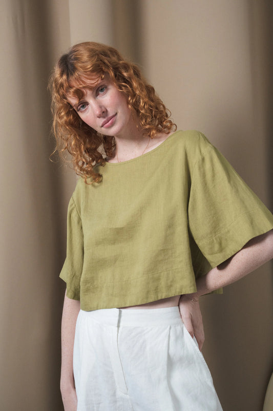 Woman wearing a green top and white pants against a beige background