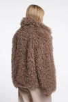 A model shown from the back wearing a shaggy, textured brown faux fur jacket and light beige trousers against a plain white background.