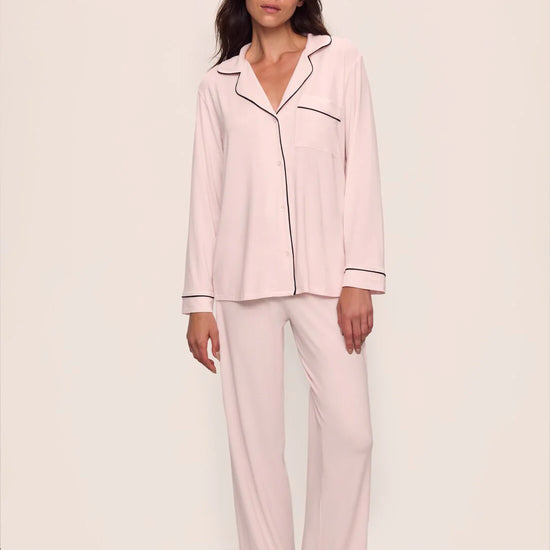 Woman wearing a pink pajama set with black piping on a white background