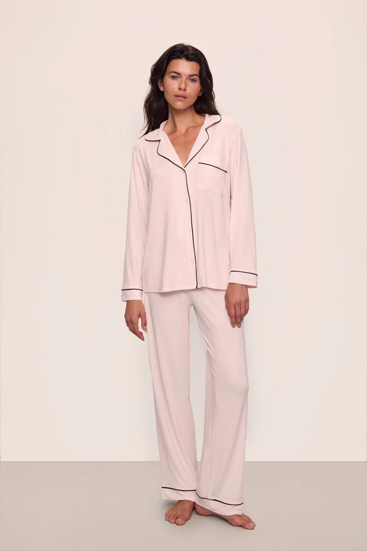 Woman wearing a pink pajama set with black piping on a white background
