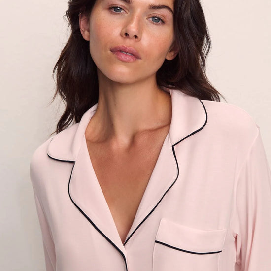 Woman wearing a light pink pajama top with black trim on a plain background