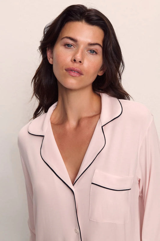 Woman wearing a light pink pajama top with black trim on a plain background