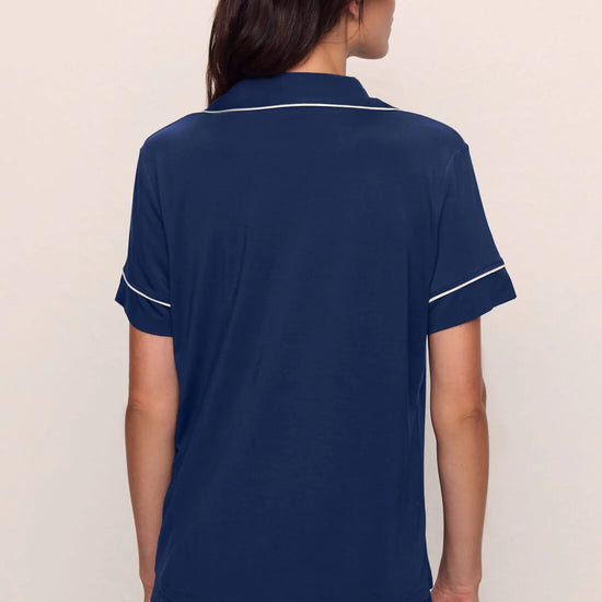 Person wearing a navy blue pajama set with white trim on a plain background from Eberjey