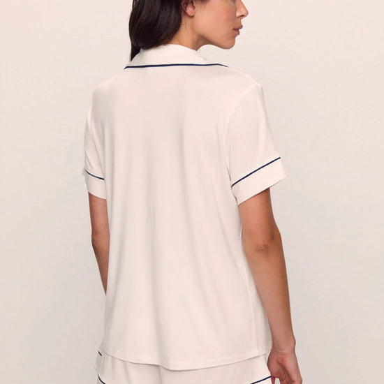 Woman wearing a white pajama set with navy trim on a plain background