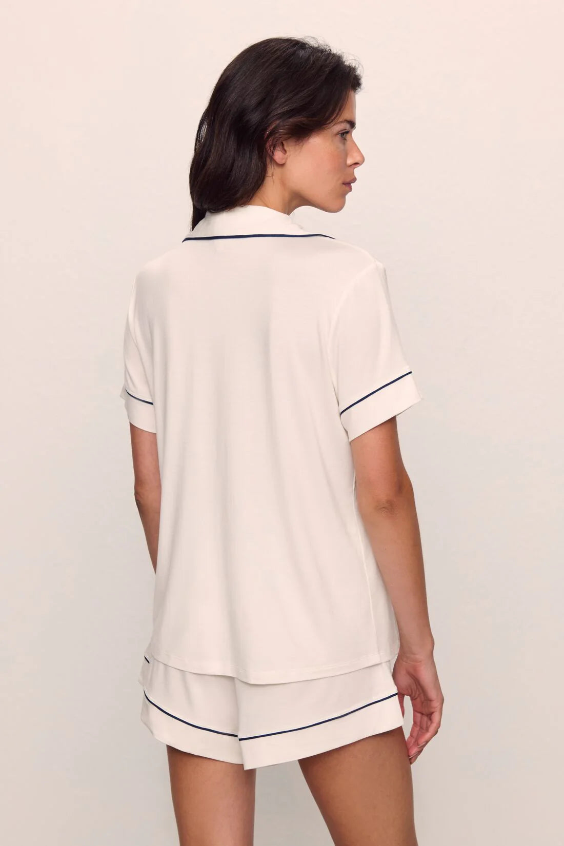 Woman wearing a white pajama set with navy trim on a plain background
