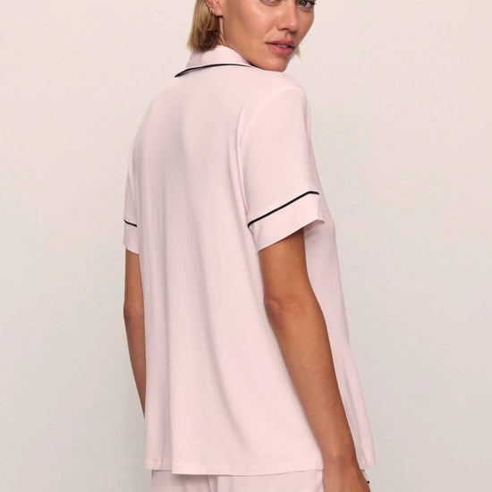 Woman wearing a pink pajama set with black piping on a plain background