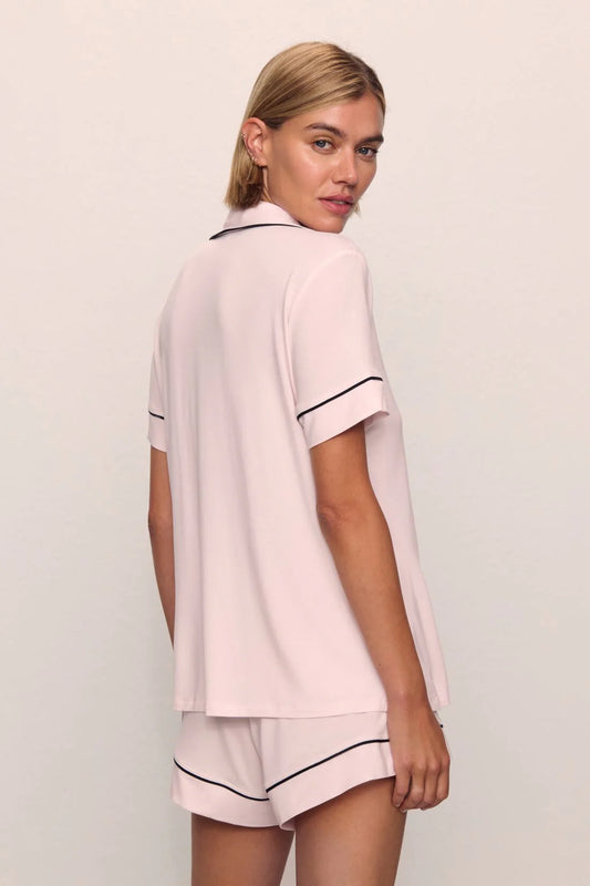 Woman wearing a pink pajama set with black piping on a plain background