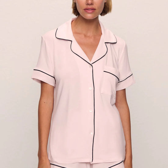 Woman wearing a pink pajama set with black piping on a plain background
