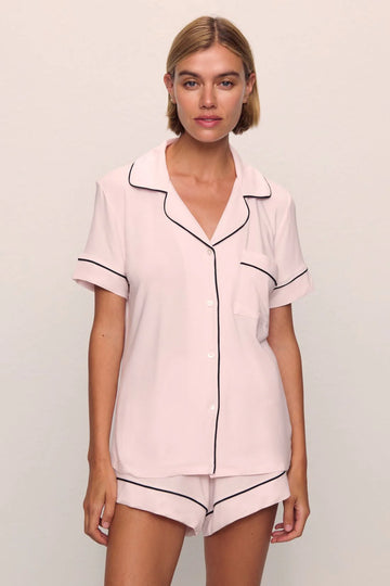 Woman wearing a pink pajama set with black piping on a plain background