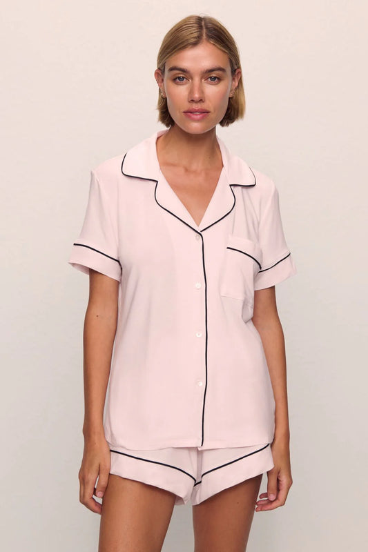 Woman wearing a pink pajama set with black piping on a plain background