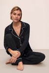 Woman wearing black pajamas with white piping sitting on a beige floor.