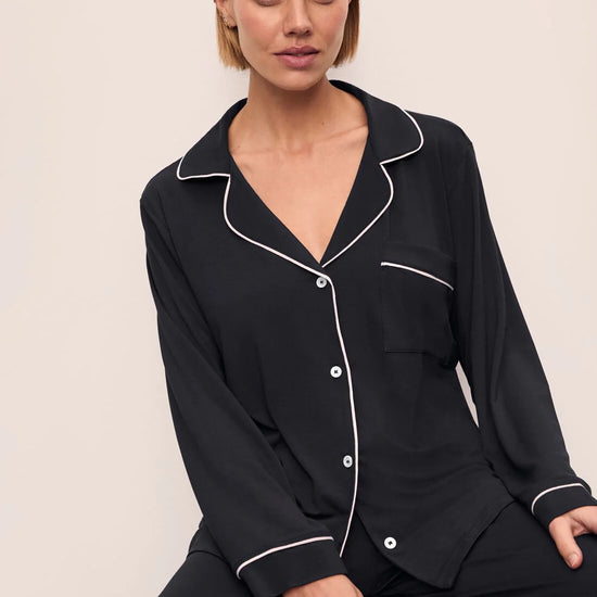 Woman wearing a black pajama set with white piping on a beige background