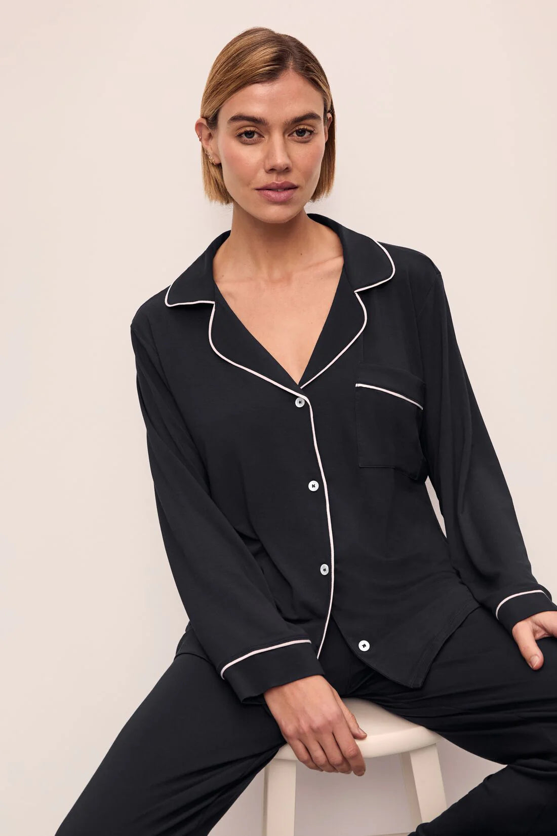 Woman wearing a black pajama set with white piping on a beige background