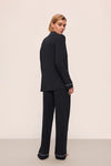 Woman wearing a black suit with white trim on a beige background