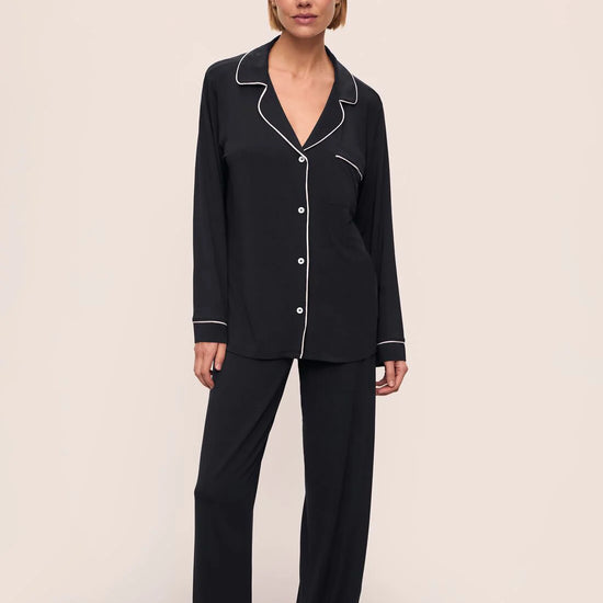 Woman wearing black pajamas with white piping on a beige background