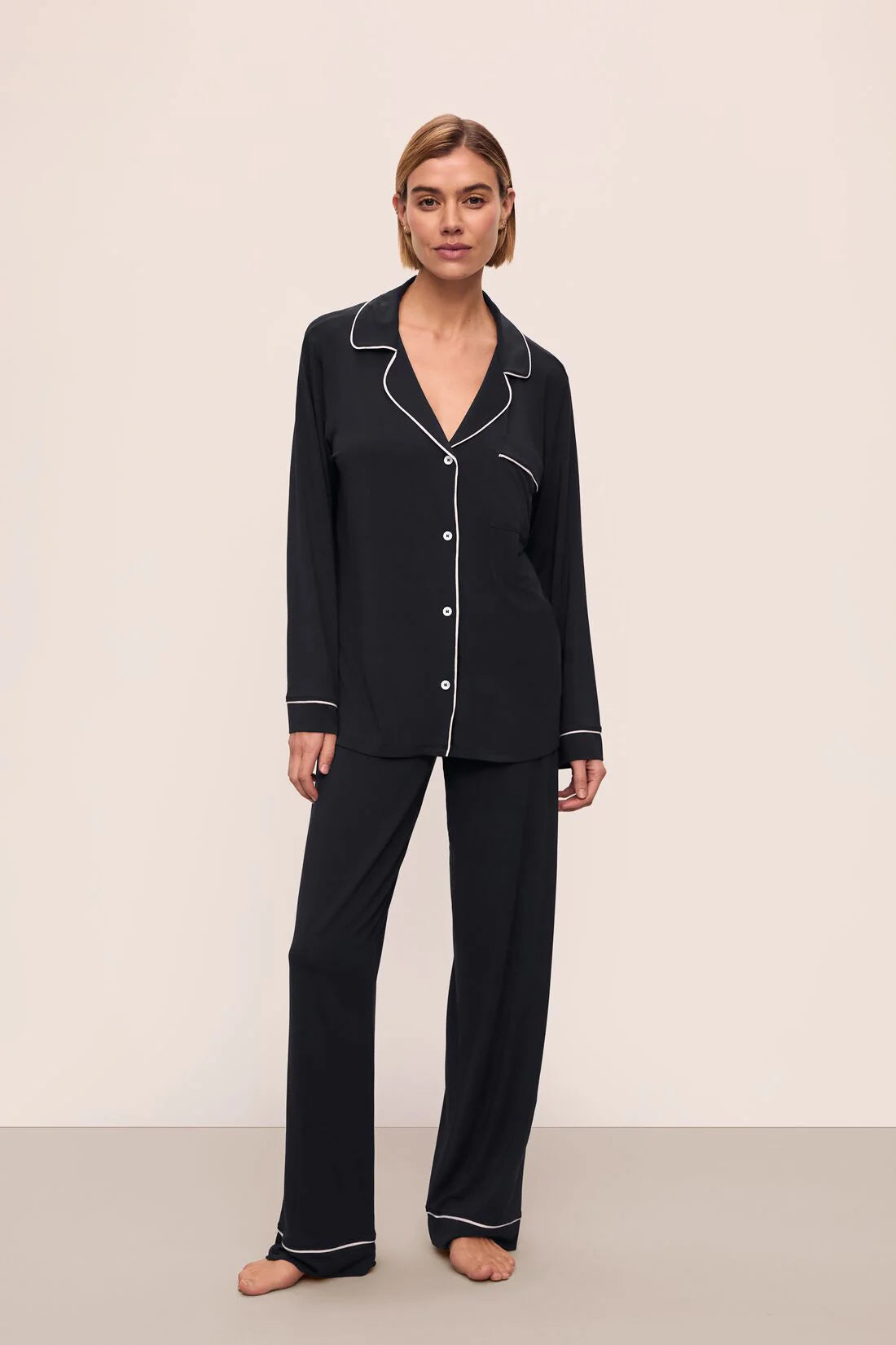 Woman wearing black pajamas with white piping on a beige background