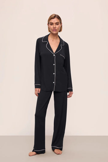 Woman wearing black pajamas with white piping on a beige background
