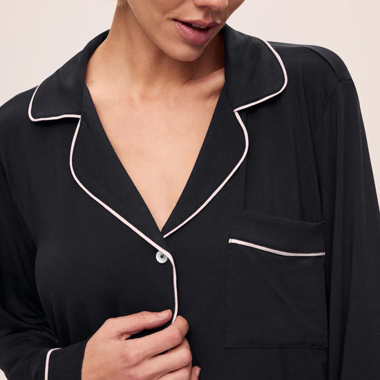 Woman wearing a black pajama top with white piping on a beige background
