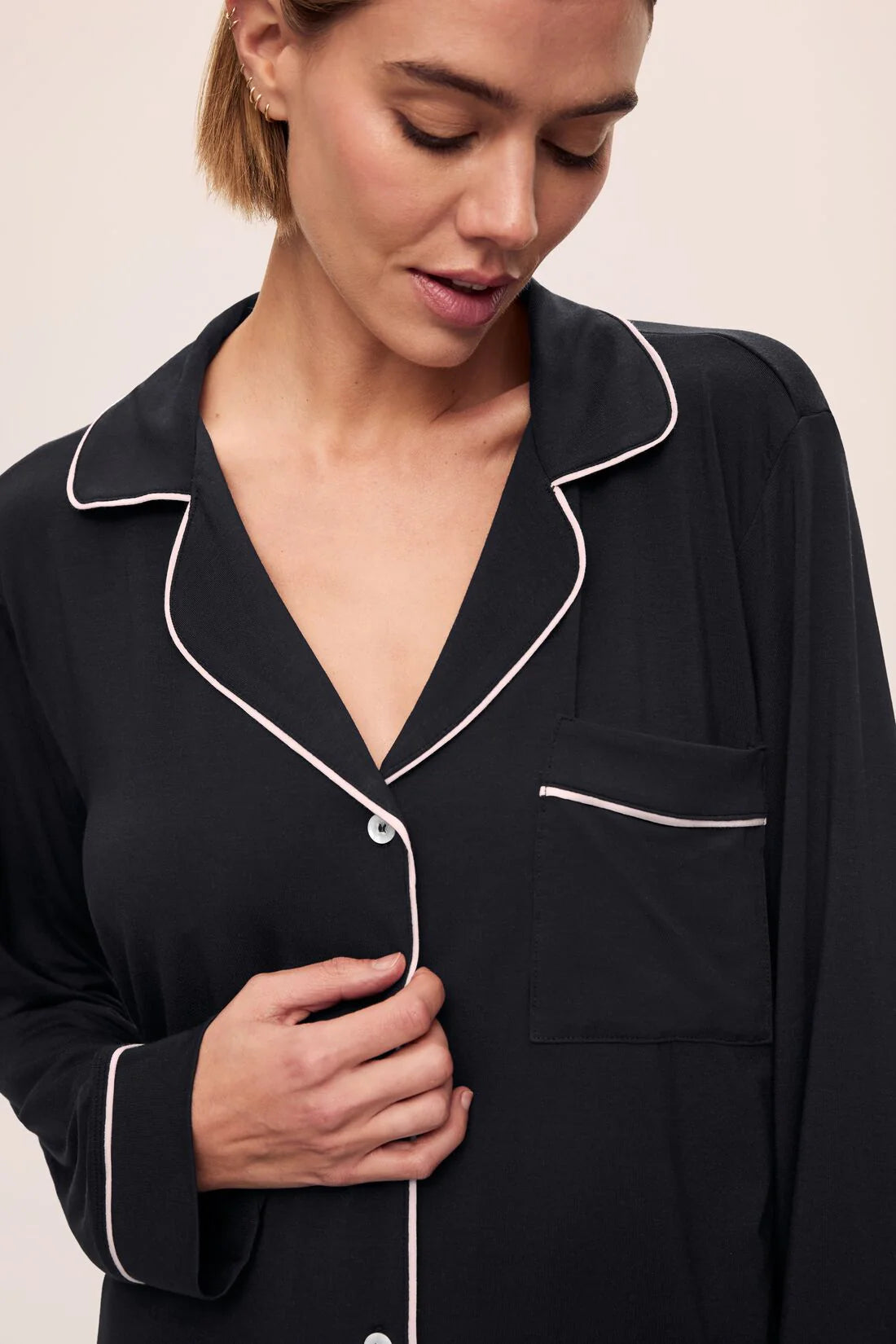 Woman wearing a black pajama top with white piping on a beige background