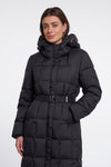 A woman wearing a long black puffer coat with a hood and a matching belt, photographed against a plain light gray studio background.