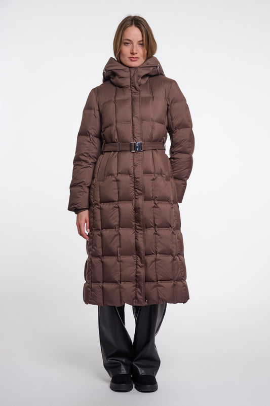 A model wearing a long, brown, quilted puffer coat with a matching belt and hood, paired with black pants, against a plain light gray studio background.