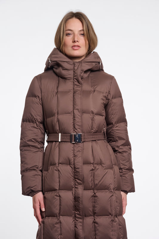 A woman wearing a long brown puffer coat with a hood and a matching belt, photographed against a plain light gray studio background.