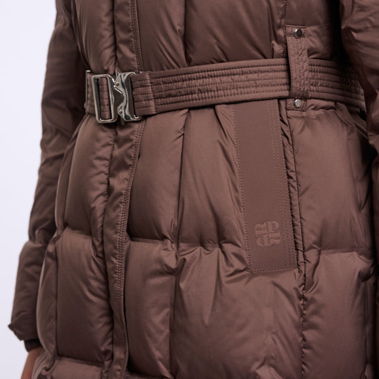 A close-up of a brown puffer coat with horizontal quilting, a matching belt with a silver buckle, and a small tonal logo patch on the side.
