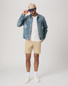 Man wearing a denim jacket, white t-shirt, beige shorts, and white sneakers on a plain background from Paige