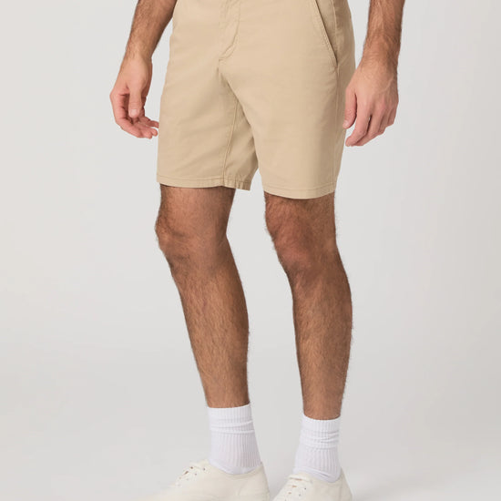 Person wearing beige shorts and white shoes on a plain background from Paige