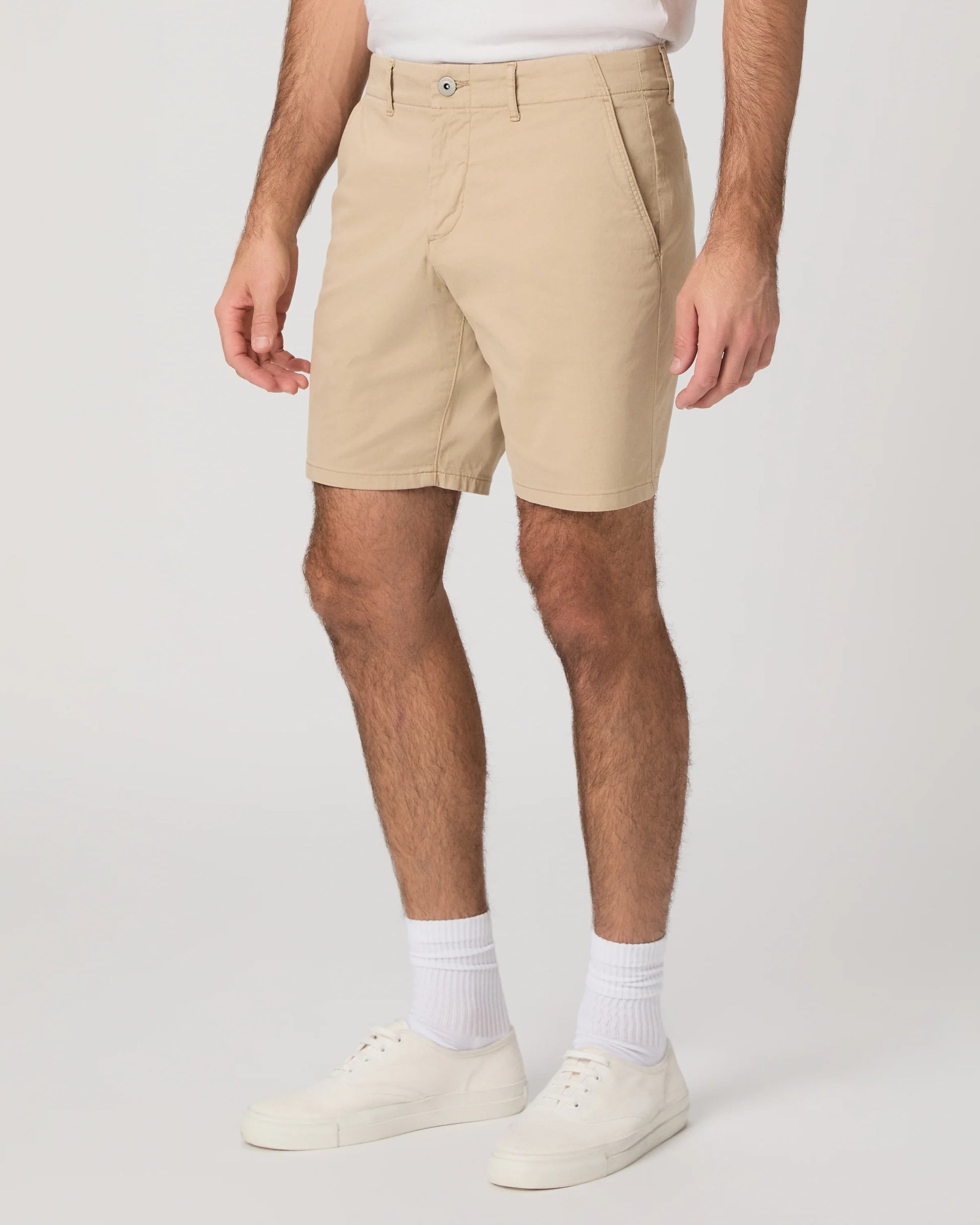 Person wearing beige shorts and white shoes on a plain background from Paige