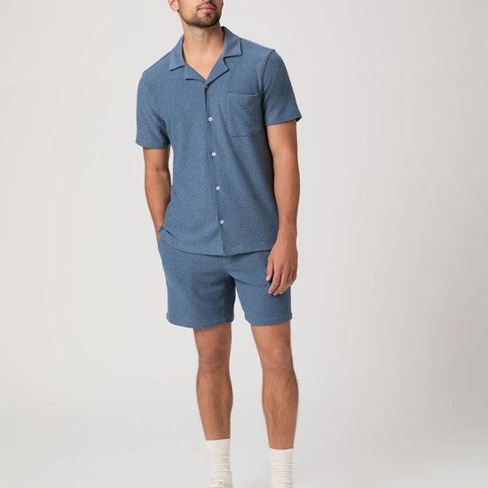 Man wearing a blue paige shirt abd matching shorts on a white background