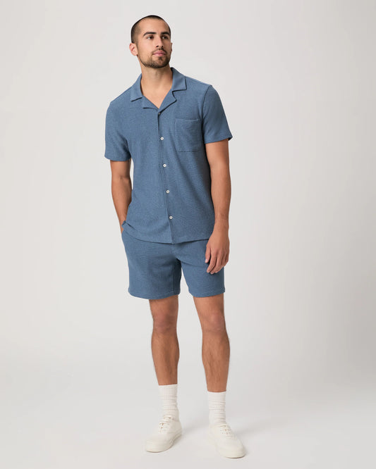 Man wearing a blue paige shirt abd matching shorts on a white background