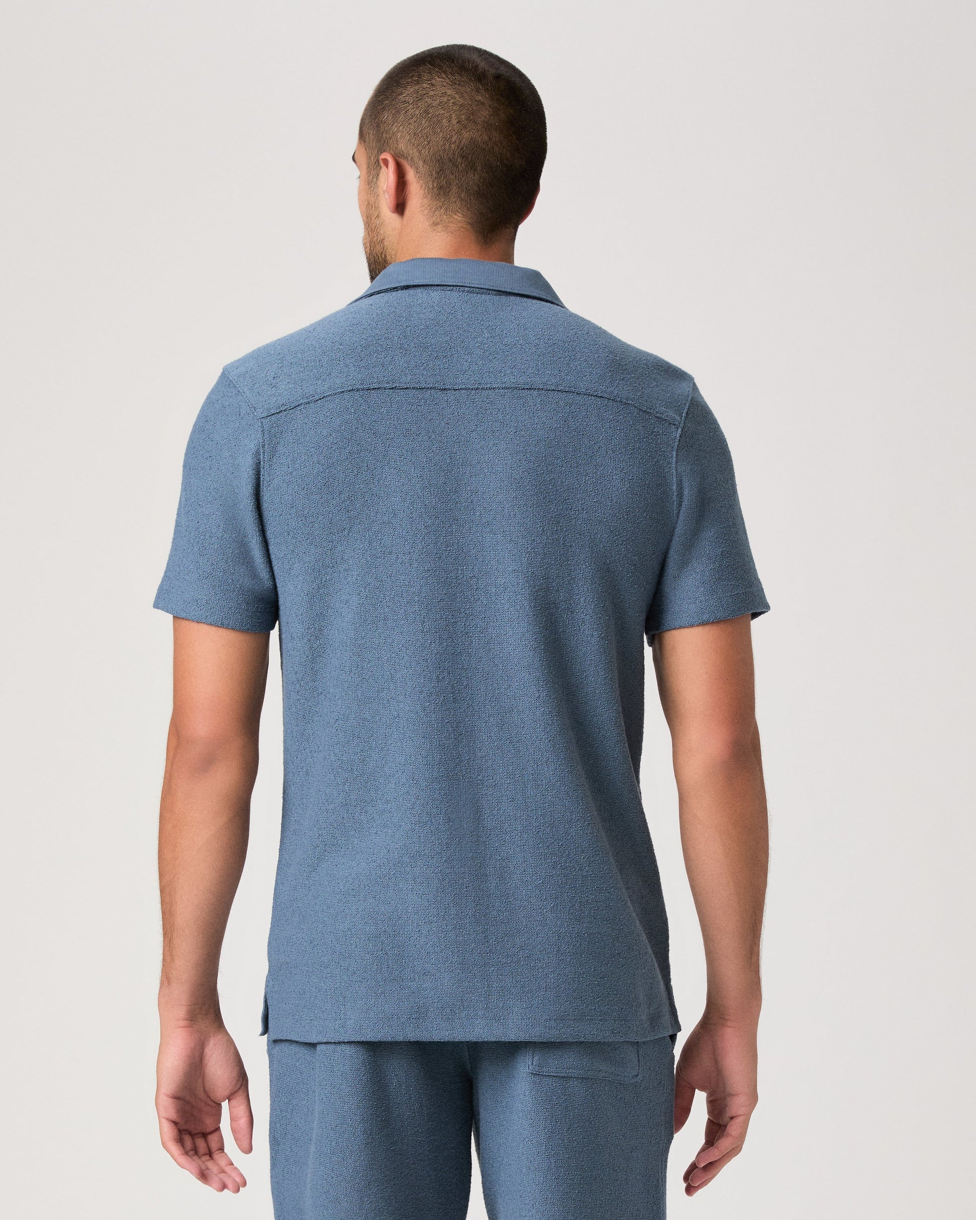 Man wearing a blue paige shirt on a white background rear view