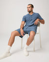 Man sat on a chair wearing a blue paige shirt and matching shorts on a white background
