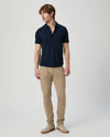 Man wearing a navy short-sleeve PAIGE shirt and beige pants on a light gray background another angle 