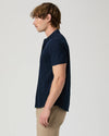 Man wearing a navy short-sleeve PAIGE shirt and beige pants on a light gray background side view