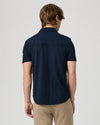 Man wearing a navy short-sleeve PAIGE shirt and beige pants on a light gray background rear view