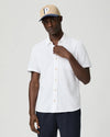 Man wearing a white short-sleeve paige shirt and beige cap with a logo on a plain background