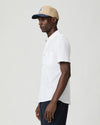 Man wearing a white short-sleeve paige shirt and beige cap with a logo on a plain background side view