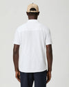 Man wearing a white short-sleeve paige shirt and beige cap with a logo on a plain background rear view