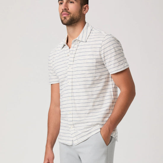 Man wearing a white striped shirt and light gray pants on a plain background